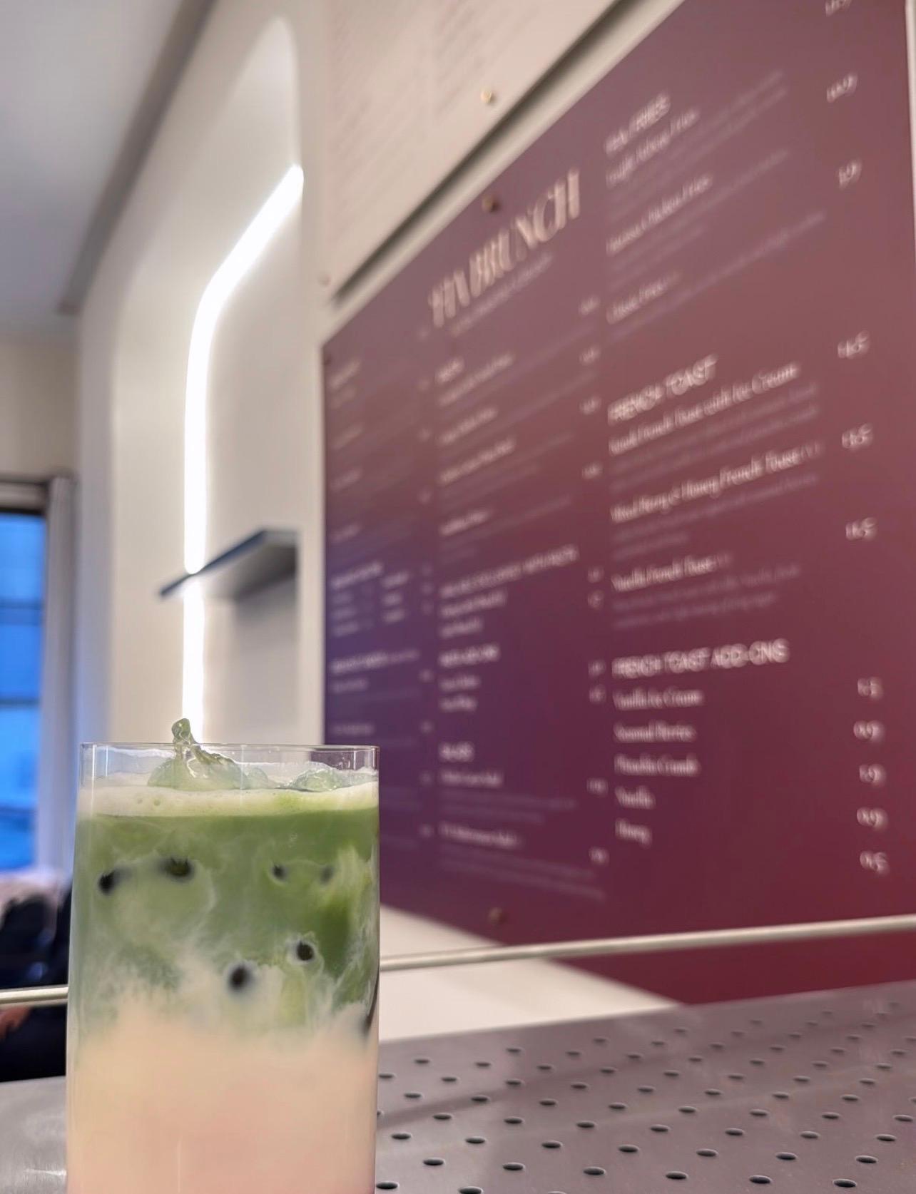 An iced matcha drink on a table at 'FIA with the brunch menu board behind