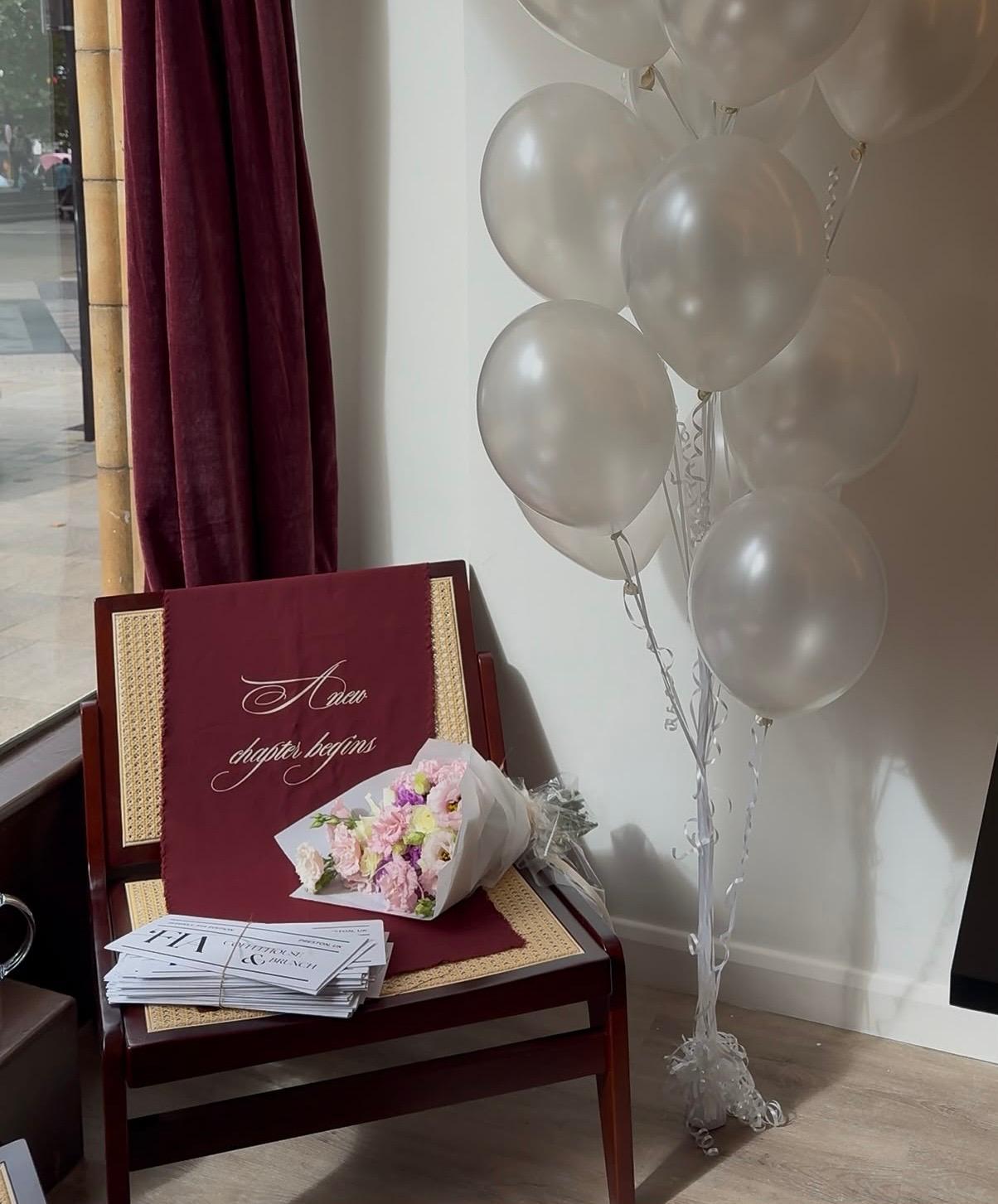 A window display at 'FIA with balloons, flowers and a 'A new chapter begins' sign