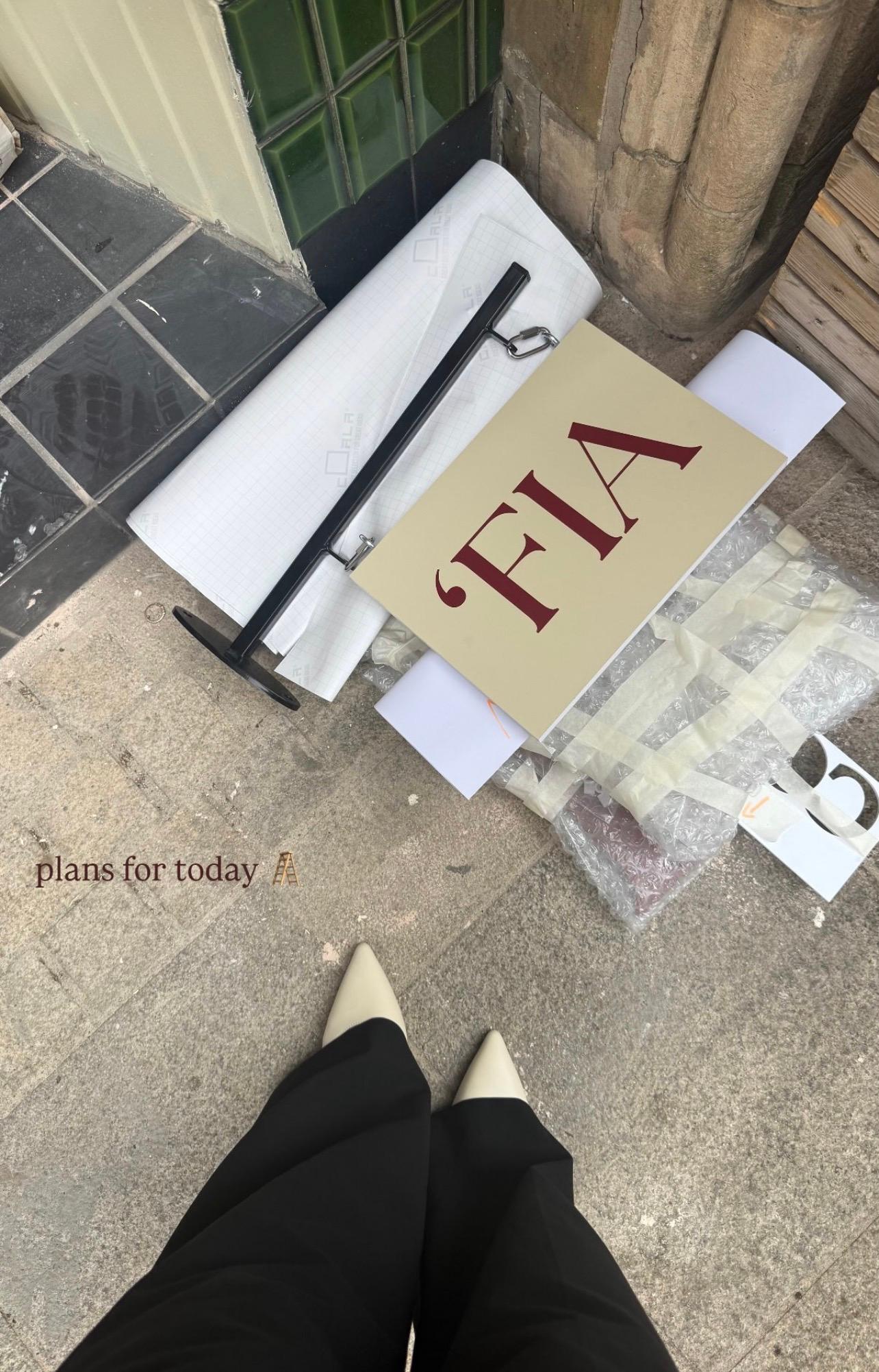 A sign leaning against the shopfront alongside rolls of vinyl lettering